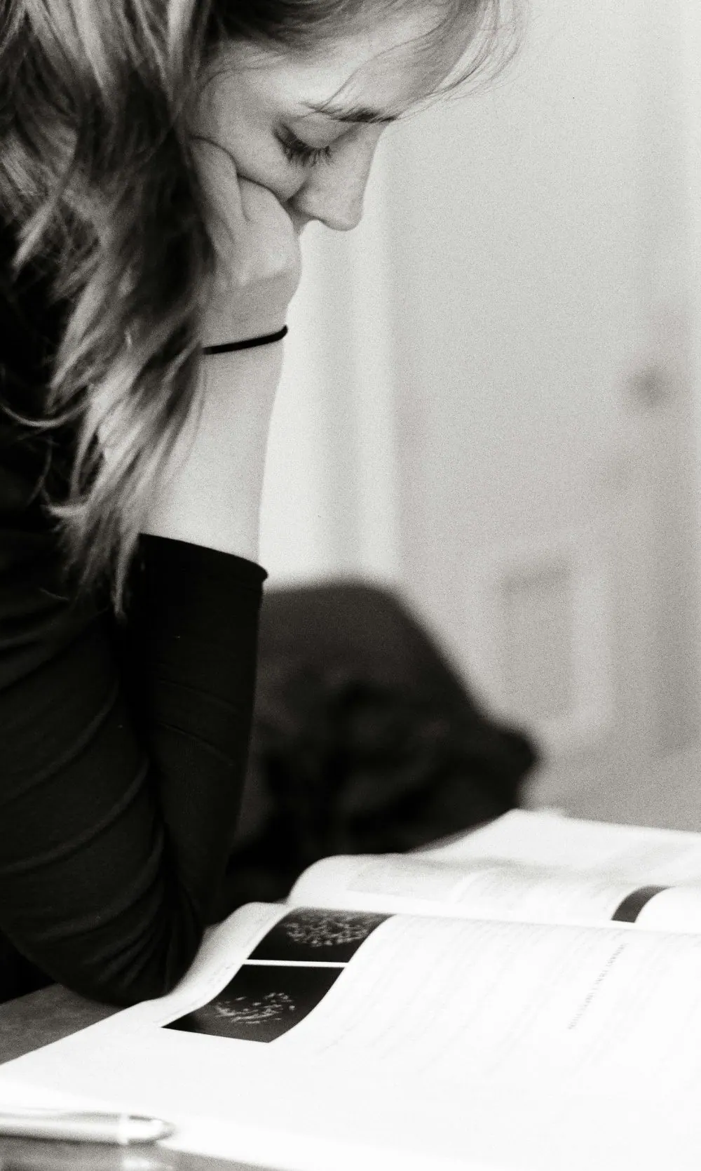 A high school student works through an open textbook, chin on her hand, in available light.